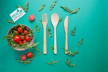 Up view of wood ecologic cutlery with 
rocket salad and tomatoes. Green background. Concept of healthy and vegan alimentation.
