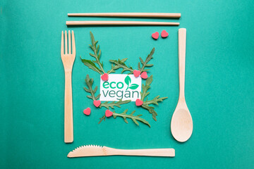 Close up of wood ecologic cutlery (fork, spoon, knife and chinese chopsticks), 
rocket salad and little red hearts. Eco vegan logo on green background. Concept of healthy and vegan alimentation. 