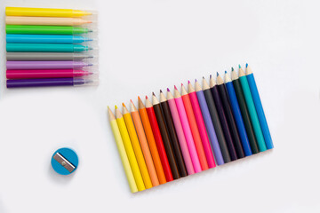 Obraz premium On a sheet of white paper are objects: sharpener, colored pencils and markers. Flatlay of school subjects.