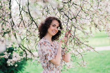 Young attractive woman with curly long hair posing in spring blooming garden, apple trees