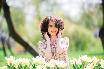 Young attractive woman with curly long hair posing in spring blooming garden, apple trees
