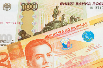 A macro image of a Russian one hundred ruble note paired up with a orange and white twenty piso note from the Phillipines.  Shot close up in macro.