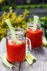 Two glasses of tomato juice with parsley and celery decorations, stand in the open air on wooden boards, the rays of the sun shine, shallow depth of field, selective focus. The concept of natural