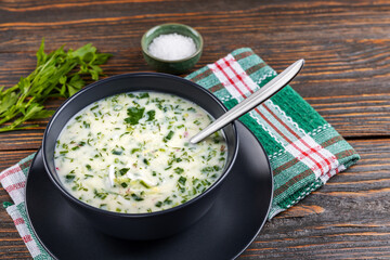 Cold soup with fresh cucumbers, radishes with yogurt in a bowl on wooden background. Traditional Russian food - okroshka. Vegetarian food. Healthy eating concept.