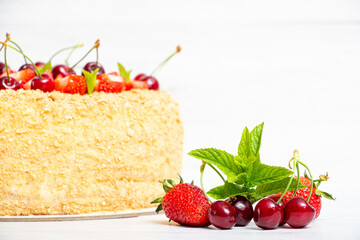 Beautiful napoleon cake with strawberries and cherries mixed with i mint on a light background