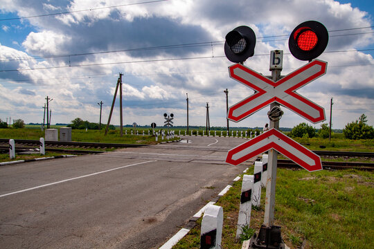 Railway crossing and traffic sign with red flashing lights against a cloudy blue sky