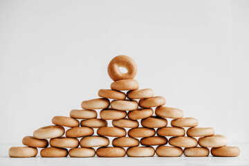 Drying or mini round bagels in the shape of a pyramid on a white wooden background. Copy, empty...