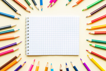 Fototapeta premium Blank notepad surrounded by multicolored pencils. Flatly.