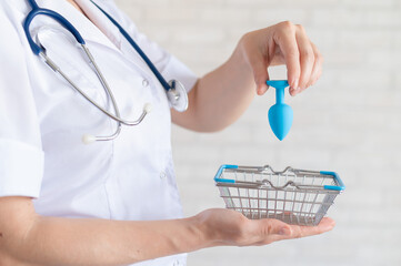 Faceless gynecologist puts anal plug in miniature shopping baskets. The doctor holds the device for...