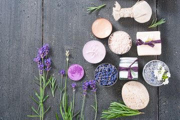 Fototapeta na wymiar beauty product samples with fresh purple and blue dried lavenders, bath salts and massage pouches on dark wood table background