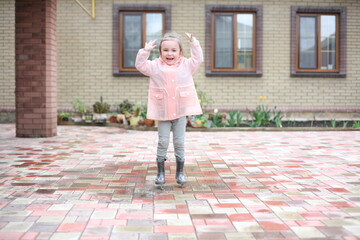 A small child is jumping in a puddle. The child is happy. The girl jumped over the puddle and raised her arms above her head.