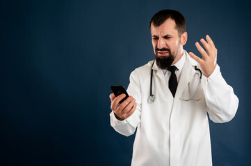 Male doctor with stethoscope in medical uniform holding smartphone, texting, looking nervously