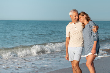 Mature, happy couple walking in each other's arms on the beach.