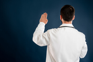 Male doctor with stethoscope in medical uniform showing oath from behind