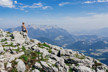 Woman sits on a rocks and enjoys beautiful and peaceful view of a valley in Bavarian Alps