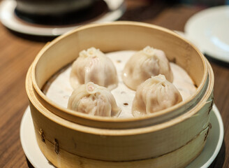 Kuala Lumpur, Malaysia - January 21, 2020 :Closeup 4 pieces of Streamed Pork Dumpings of Shanghai Xiao Long Bao serve in traditional round bamboo basket.