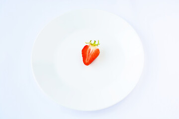 Half ripe strawberries in the center of a white plate, on a white background