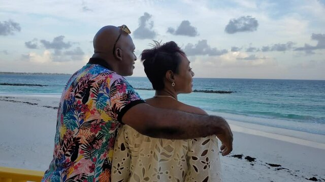 Beautiful Black African American married couple spends romantic evening at tropical island beach sunset in love / kiss scene in Caribbean