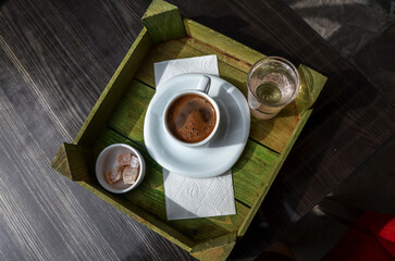 Cup of traditional turkish coffee with turkish delight and glass of water on a wooden tray