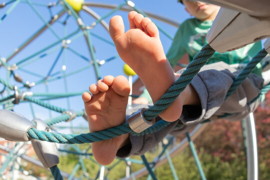 Young boy sits on a Rope Web in the playground. Feet close up.