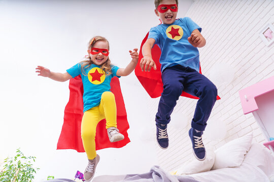 cute little girl and boy jumping from bed to fly, play superhero