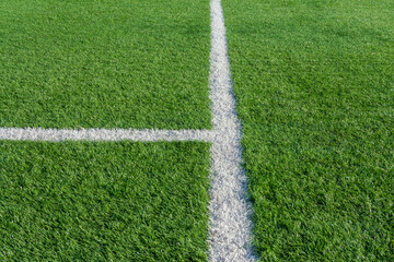 Green grass and white border lines on football ground. Soccer field on artificial turf. Artificial green grass texture. Artificial football field in an open stadium
