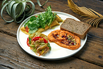 Healthy breakfast - omelet with kimchi and baked peppers hummus in a plate on a wooden background