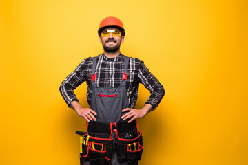 Portrait of happy handyman with tool belt isolated on yellow background