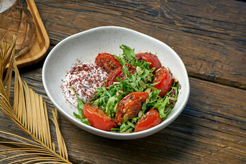 Vegetarian salad with baked tomatoes, greek yogurt and arugula in a bowl on a wooden background