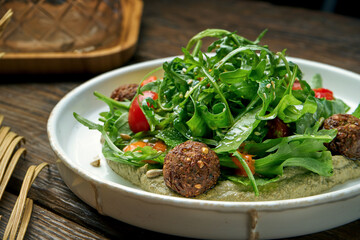 Appetizing vegetarian salad with arugula, falafel, cherry tomatoes and hummus on a wooden background