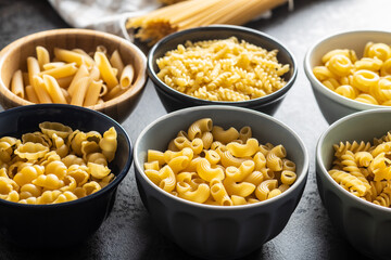 Various types of raw italian pasta in bowls.