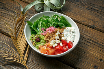 Superfood - a bowl with rice, salmon, guacamole, poached egg and cherry tomatoes seasoned with Greek yogurt on a wooden background. Balanced food