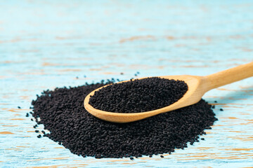 organic seeds of black cumin in a wooden spoon  on a rustic table.