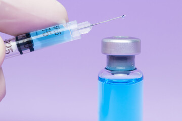 hand with glove holding a syringe with a liquid drop and a medical bottle with blue liquid