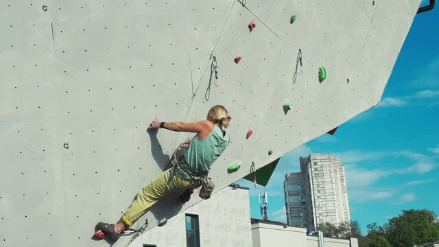 Young woman rock climber climbing on artificial rock wall in outside climbing gym. sports woman working out on extrime sport route. strength, conquering and training concept
