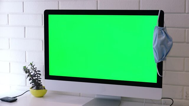 Close Up Green Screen Computer With Face Mask Hanging, Zoom In. Close up green screen computer on desktop with protective face mask hanging. Zoom In