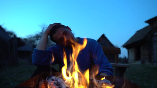 A man prepares a barbecue. A man roasts meat on a fire. A man is sitting near a fire in the forest. Picnic in nature. Self-isolation.