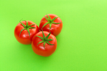 Three red real tomatos seen at its top on a green background