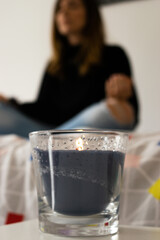 Photo of a candle and at the background a girl meditating