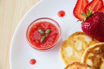 Three pancakes with cheese and strawberries and sauce on a white dish against wood background. Delicious cheese pancake and strawberries for the breakfast or lunch. Tasty meal with berries.