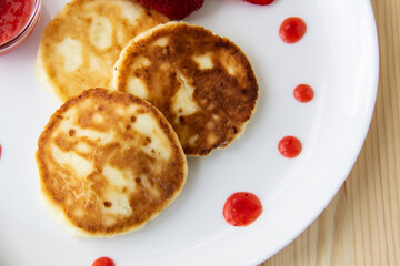 Three pancakes with cheese and strawberries and sauce on a white dish against wood background. Delicious cheese pancake and strawberries for the breakfast or lunch. Tasty meal with berries.