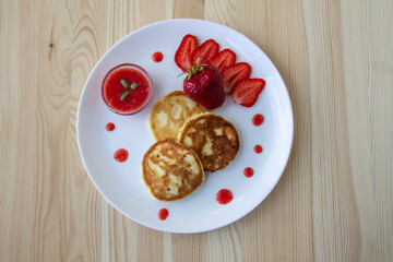 Three pancakes with cheese and strawberries and sauce on a white dish against wood background. Delicious cheese pancake and strawberries for the breakfast or lunch. Tasty meal with berries.