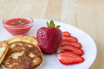 Three pancakes with cheese and strawberries and sauce on a white dish against wood background. Delicious cheese pancake and strawberries for the breakfast or lunch. Tasty meal with berries.