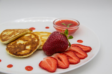 Three pancakes with cheese and strawberries and sauce on a white dish against wood background. Delicious cheese pancake and strawberries for the breakfast or lunch. Tasty meal with berries.