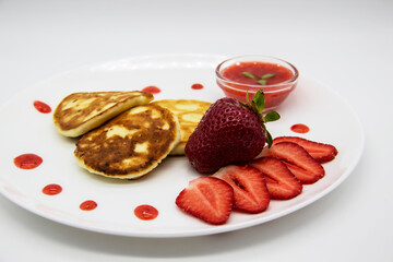 Three pancakes with cheese and strawberries and sauce on a white dish against wood background. Delicious cheese pancake and strawberries for the breakfast or lunch. Tasty meal with berries.