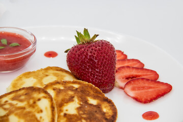 Three pancakes with cheese and strawberries and sauce on a white dish against wood background. Delicious cheese pancake and strawberries for the breakfast or lunch. Tasty meal with berries.