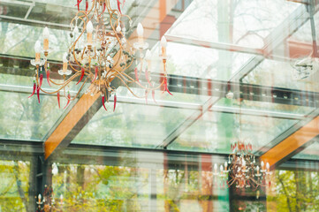 Crystal chandeliers with small decorative peppers under the glass roof of the restaurant in the park. Restaurant interior seen through the glass.