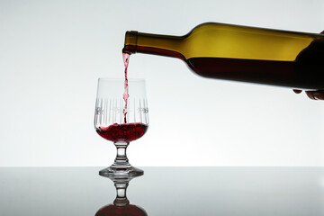 red wine is pouring into a glass from a bottle on white background