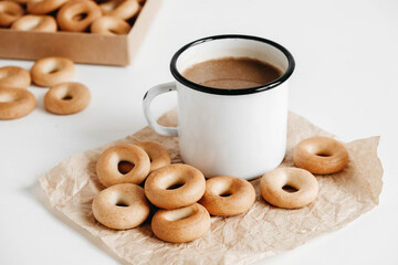 Metal mug with hot drink and mini round bagels on a white wooden background. Copy, empty space for text