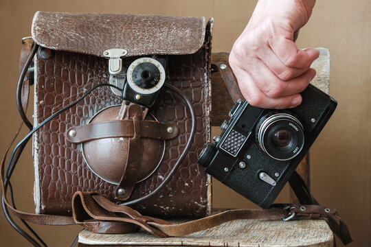 Old film camera in the photographer's hand. Next to a bag with a flash. Old photography technology.